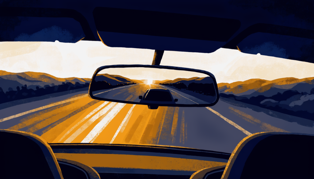Rear-view mirror at dusk showing the road behind while the road ahead opens through the windshield