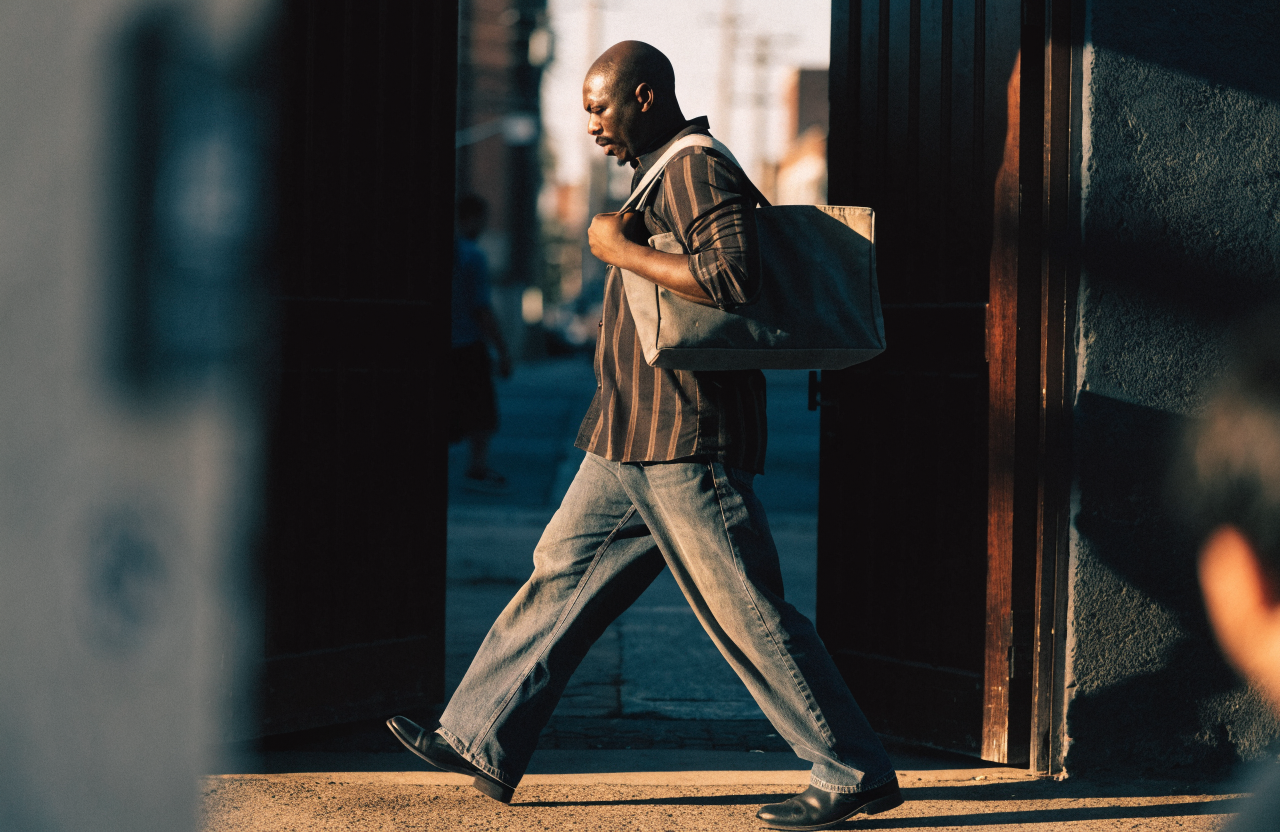 A Black man walking purposefully out of a doorway into morning light