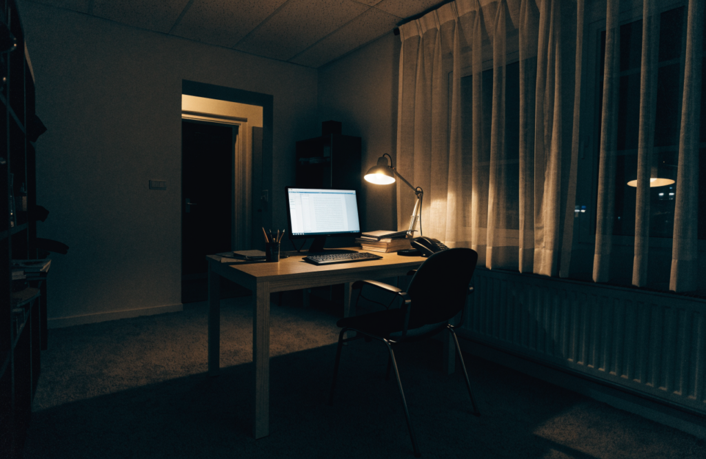 An empty home office at night, one monitor glowing on a desk, nobody in the chair