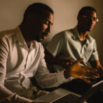 One man teaching another how to use a tool on a laptop