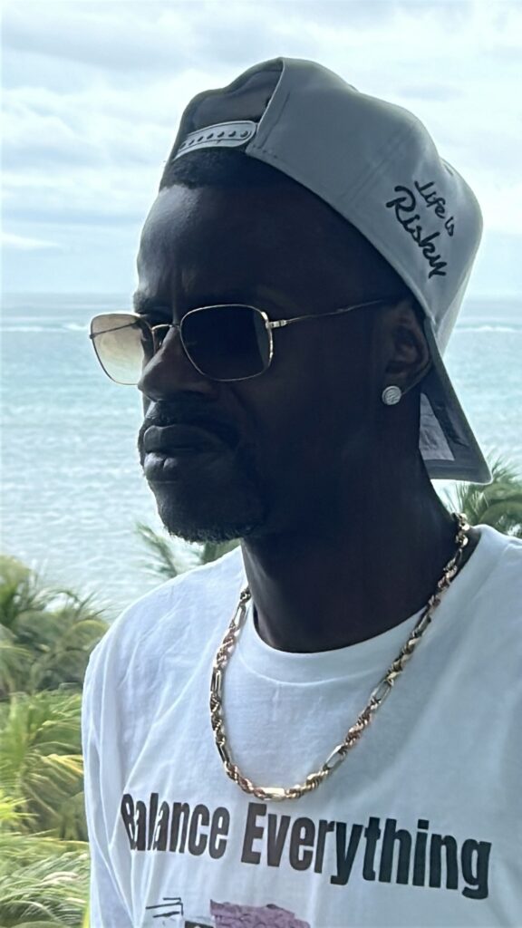 David Hawkins on a balcony in San Pedro, Belize, with the Caribbean and palm trees behind him