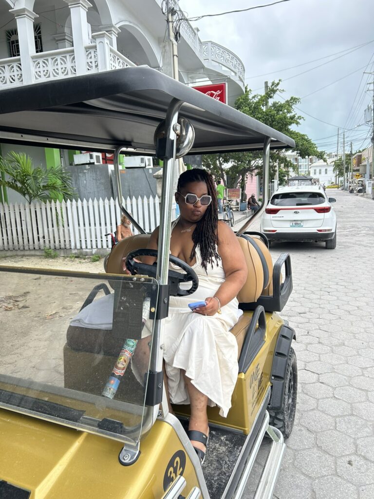 A yellow golf cart on a street in San Pedro, Belize, with a car passing behind it