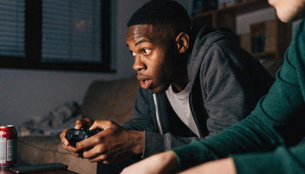 A young man leaning forward on a couch mid-match with a game controller in both hands